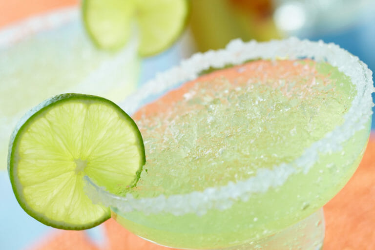 Close-up of a glass of chilled lime margarita rimmed with coarse sugar and a lime slice garnish.