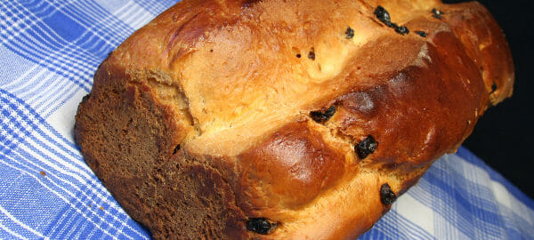 A browned loaf of Sweet Potato Bread with raisins, placed on a blue plaid tablecloth.