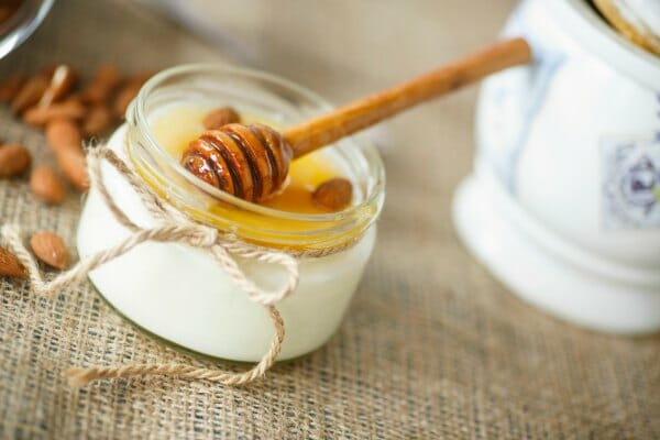 A small glass jar of yogurt with honey and a wooden honey server on top.