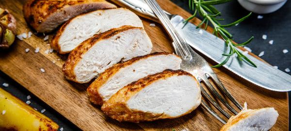 A wood cutting board with slices of Air Fried Chicken, a knife and fork, and ramekins filled with dipping sauces.