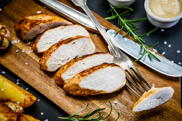 A wood cutting board with slices of Air Fried Chicken, a knife and fork, and ramekins filled with dipping sauces.
