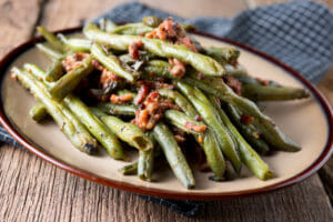 A brown rimmed plate with a serving of Bacon Green Beans.