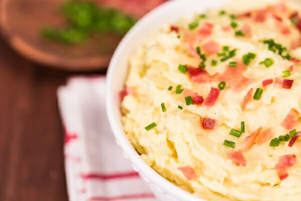 Close-up of a white bowl filled with Bacon Horseradish Mashed Potatoes, topped with chives and bacon pieces.