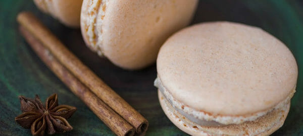 A green plate with three Cinnamon Macarons, a cinnamon stick, and star anise.