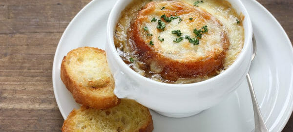 A white cup of French Onion Soup, topped with melted cheese and crusty bread.