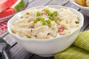 A white bowl filled with German Potato Salad topped with chopped green onions.