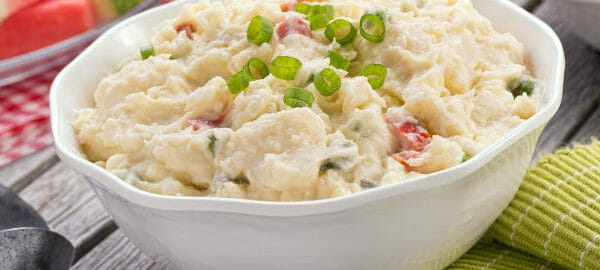 A white bowl filled with German Potato Salad topped with chopped green onions.