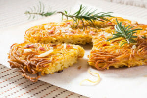 Golden spaghetti pie on parchment paper, with one cut slice, topped with sprigs of rosemary.
