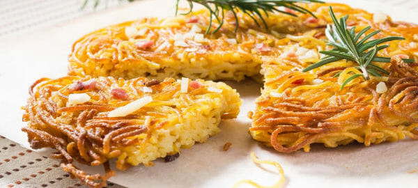 Golden spaghetti pie on parchment paper, with one cut slice, topped with sprigs of rosemary.