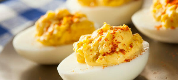 Spicy Dijon Deviled Eggs topped with paprika, placed on a gold platter.