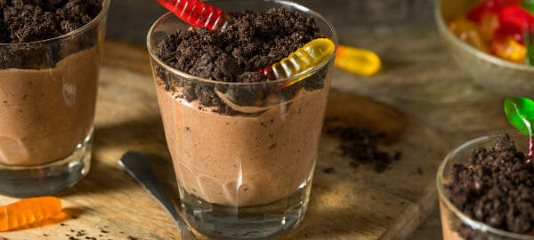 Three short glasses filled with Dirt Dessert, a chocolate pudding topped with crushed chocolate cookies and gummy worms.
