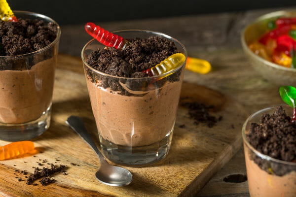 Three short glasses filled with Dirt Dessert, a chocolate pudding topped with crushed chocolate cookies and gummy worms.