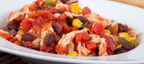 A white bowl filled with colorful Fiesta Chicken, with beans, tomato chunks, and corn.