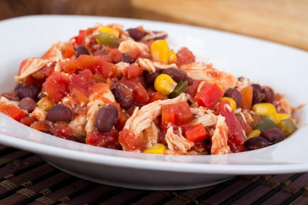 A white bowl filled with colorful Fiesta Chicken, with beans, tomato chunks, and corn.