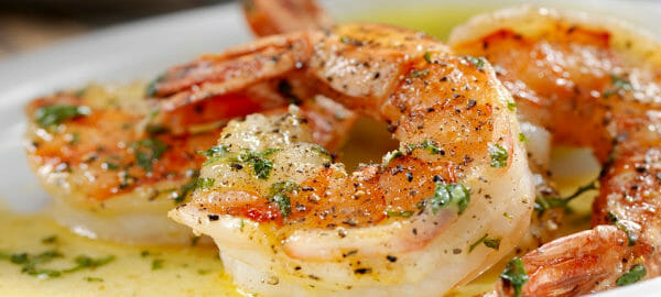 A white plate with a serving of shrimp topped with melted butter and parsley flakes.