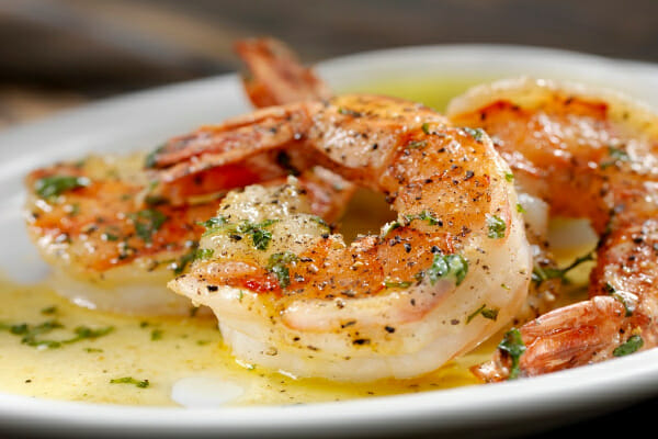 A white plate with a serving of shrimp topped with melted butter and parsley flakes.