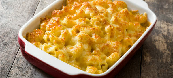 A red and white casserole dish filled with baked Macaroni and Cheese.