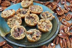 A multicolor blue plate with Pecan Pie Muffins, surrounded by whole pecans.
