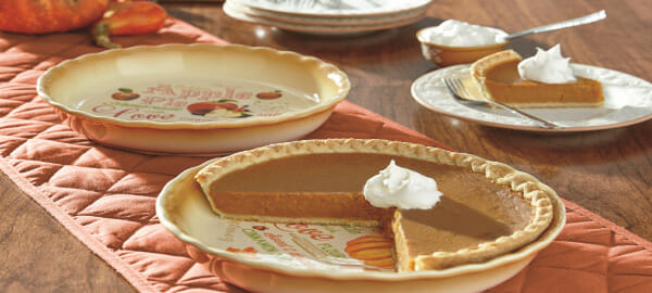 An orange table runner with two pie plates, one filled with pumpkin pie, and a slice topped with whipped cream.