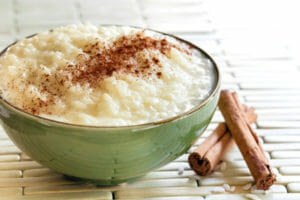 A green bowl filled with rice pudding topped with cinnamon, with two cinnamon sticks nearby.