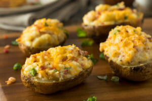 Four Twice Baked Potatoes on a wooden cutting board, topped with chopped green onions.