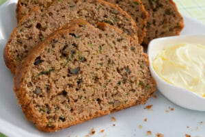 Close-up of slices of Zucchini Bread on a white plate, with a ramekin of whipped butter.