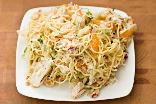 A square white plate filled with Chinese Chicken Salad with noodles and Mandarin oranges.
