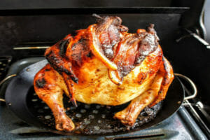 A glazed whole chicken on a broiler pan placed on a grill.