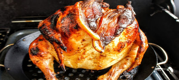 A glazed whole chicken on a broiler pan placed on a grill.