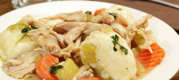 A white bowl filled with chicken and dumplings, including carrot and celery slices.