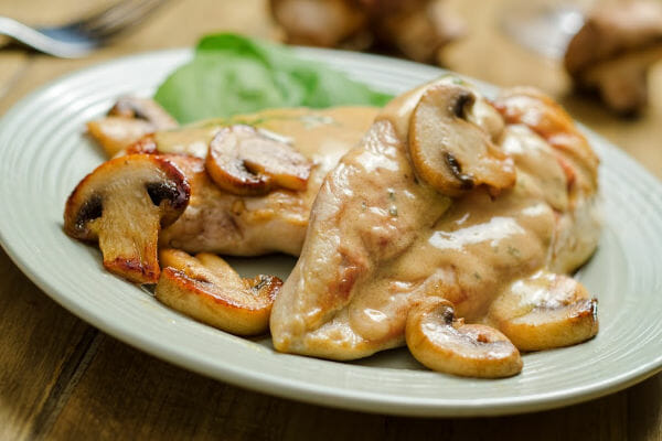 A white plate with a serving of chicken breasts topped with mushroom gravy and mushroom slices.