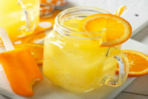 A Mason jar mug filled with Creamsicle Ice and a sliced orange garnish, next to an Orange Creamsicle ice cream bar.