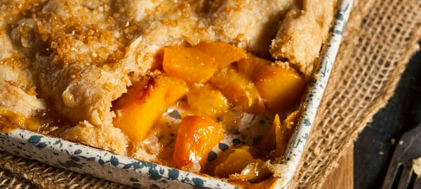 A green and white spatter baking pan filled with Peach Cobbler, with one piece removed.