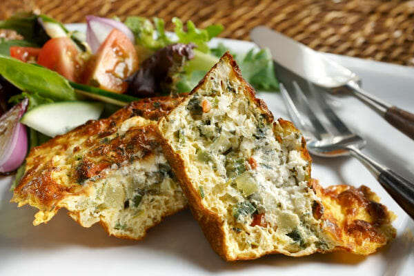 A white plate with a serving of Quiche Pie, a mixed lettuce salad, and a fork and knife.