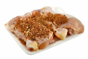 A square plate with four raw chicken legs topped with a dry rotisserie rub.