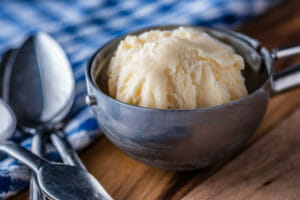Close-up of homemade vanilla ice cream in an ice cream scoop, next to spoons and a blue check towel.