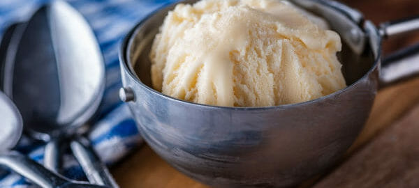 Close-up of homemade vanilla ice cream in an ice cream scoop, next to spoons and a blue check towel.
