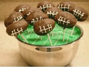 Cake pops in the shape of footballs stuck in a field of green frosting.