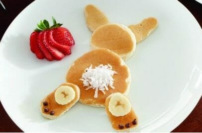 A white plate with small pancakes arranged in the shape of a bunny, with a side of sliced strawberries.